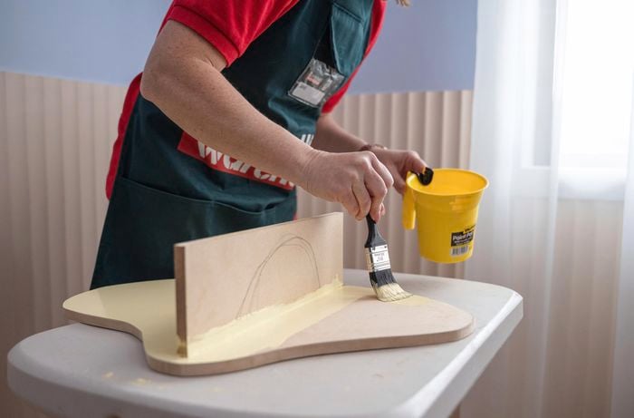 A person painting a wooden shelf using a paint brush.