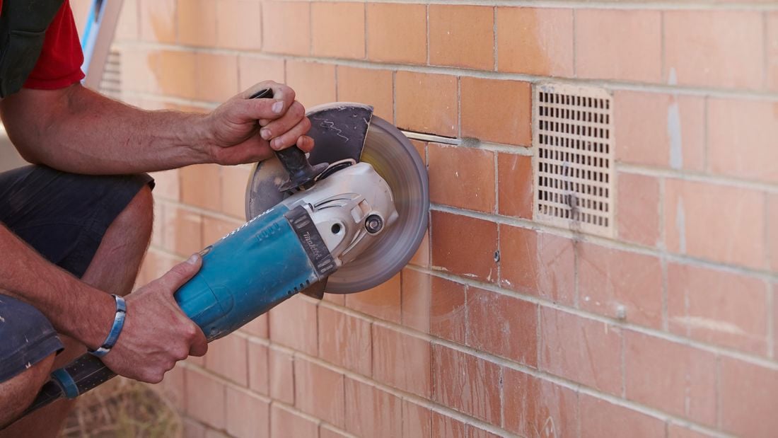An angle grinder being used to cut vertical lines into a brick wall