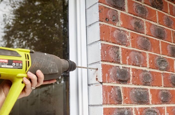 A hole being drilled in brickwork around a window