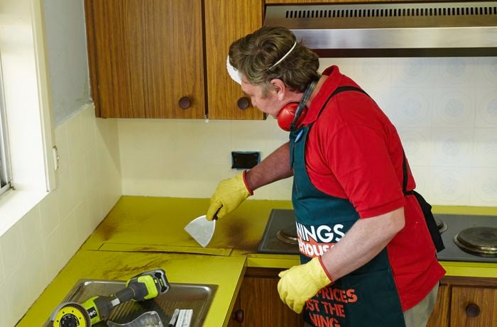 Person using scraper to remove bit of benchtop that has been cut.
