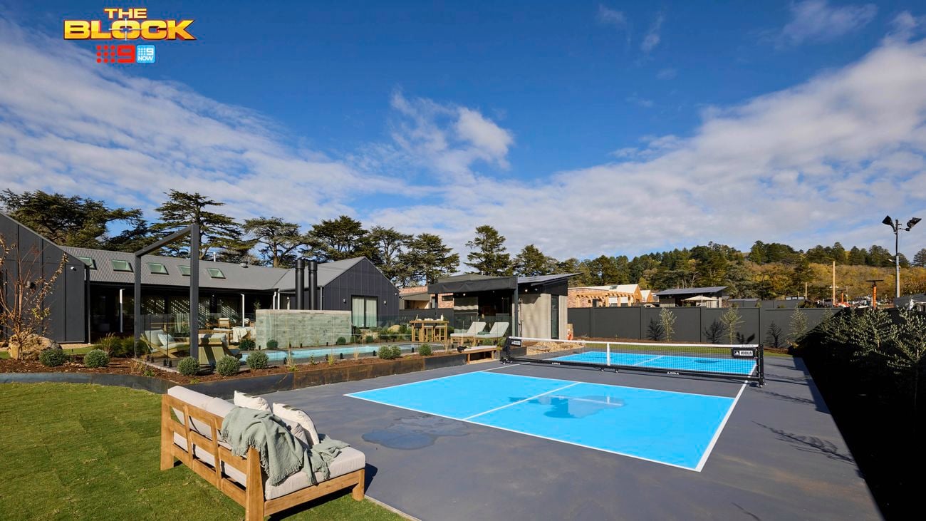 The back of a house with a blue court with a net, outdoor lounge, a pool, outdoor room and plants in it.