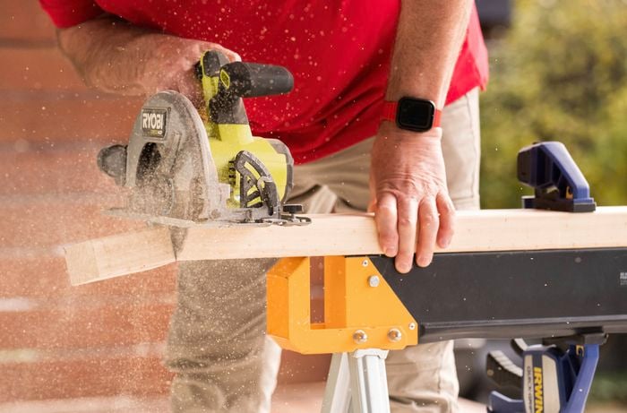A person in a red t-shirt is cutting a timber block with a circular saw to begin building the raised platform for your cabinets. 