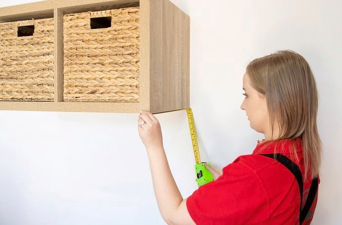 Person using tape measure to measure distance on shelf