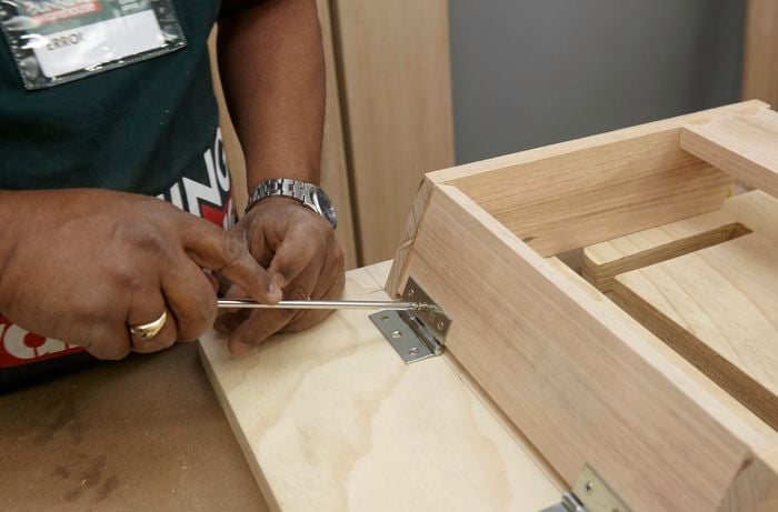 Person screwing hinge into upside down DIY wooden step stool.