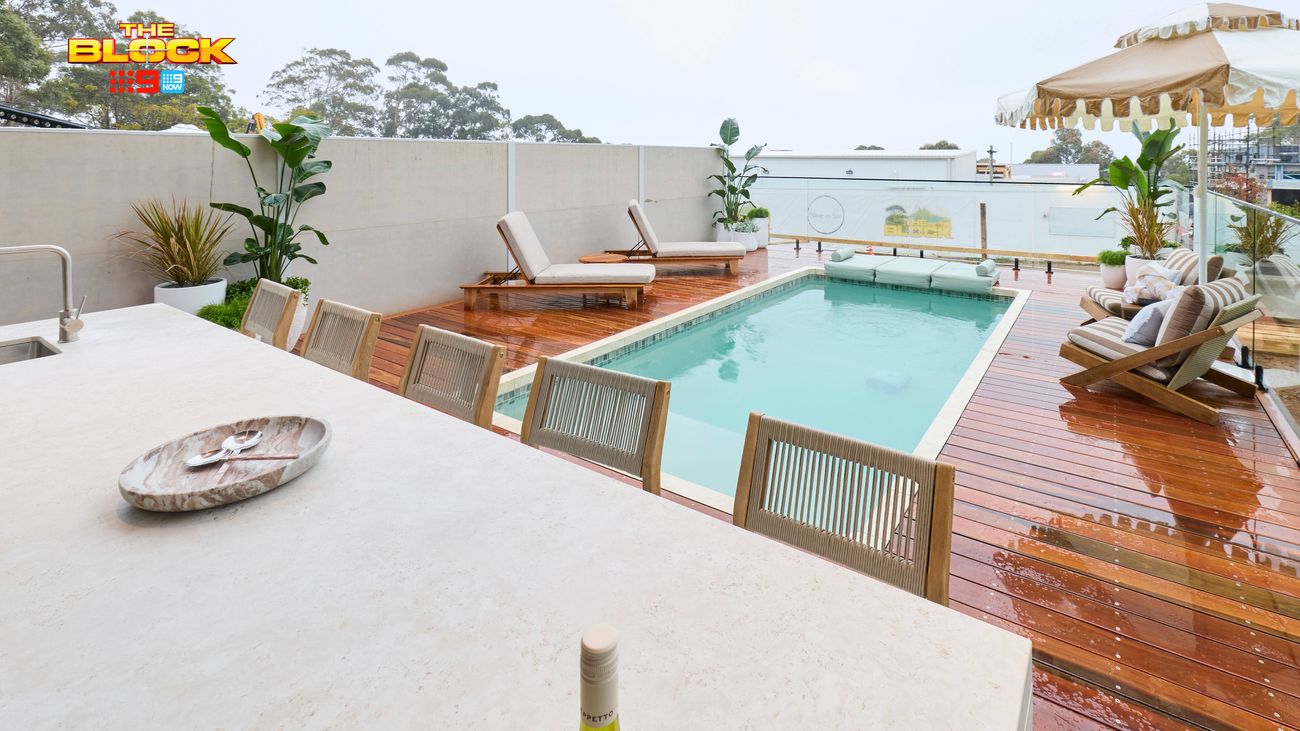 Outdoor pool and entertaining area featuring timber decking, sun loungers, tropical plants and a large dining table.