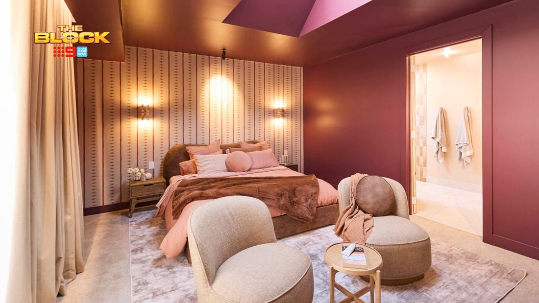 Bedroom with plum-colored walls, upholstered bed, two beige chairs, and soft lighting.