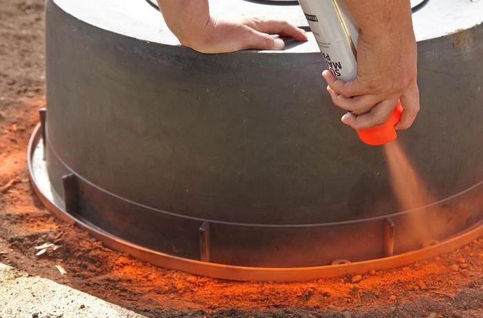 A person using spray paint to mark the ground around an inverted plastic tub