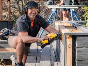 A tradesperson wearing safety glasses and using a DeWALT nail framer on an outdoor deck.