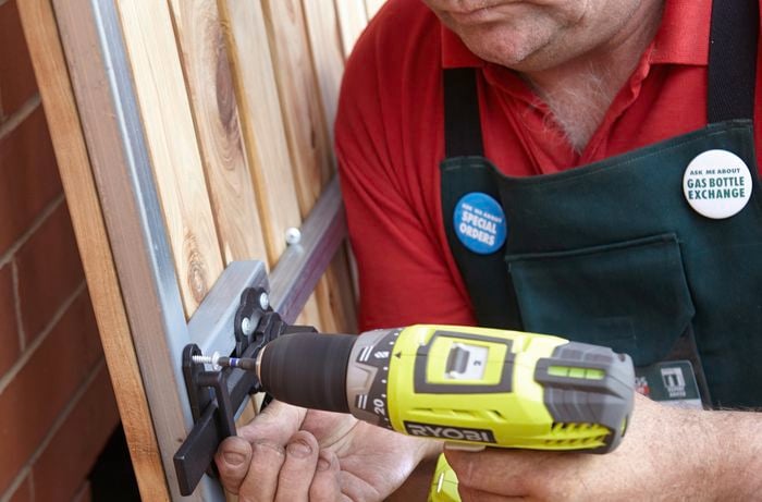 Person screwing a latch keeper to a gate using a cordless driver