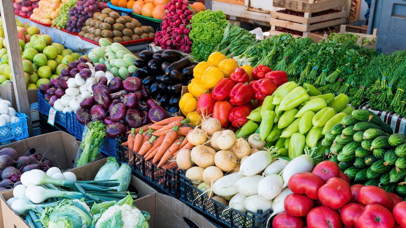 A close-up of brightly-coloured fruits, vegetables and green herbs displayed on a farmer’s market stand.