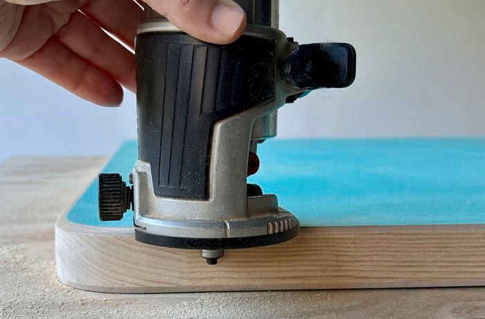 Close up of a hand using a trim router on the edges of a door panel.