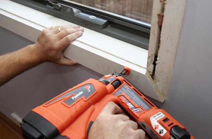 A person attaching architrave under a window with a nail gun