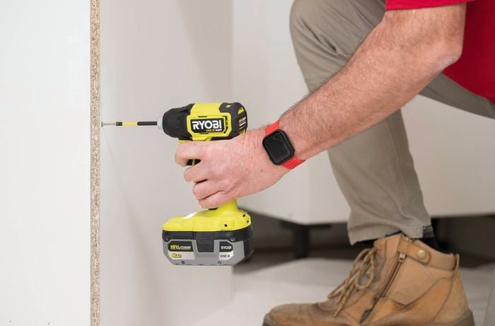 A person is using a power drill to fix the back panel to the base using the screws.