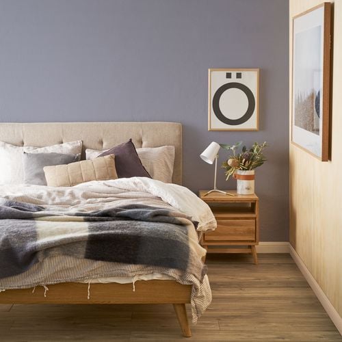 Detail of bedroom painted mauve with wooden furniture and natural toned bedding