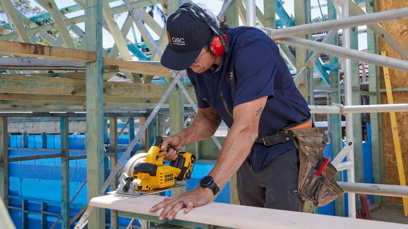Stuart Quine smiles to camera while using a cordless DeWALT circular saw on a jobsite