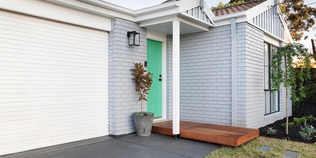 Exterior of a brick house, painted white and featuring a green door.
