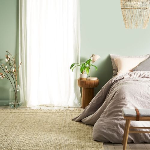 Detail of bedroom painted pale green with wooden furniture and natural tone rug and bedding