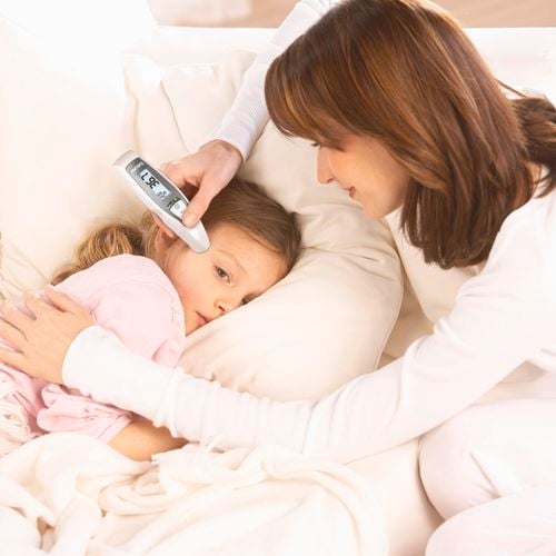 A lady taking the temperature of a child that is lying in bed