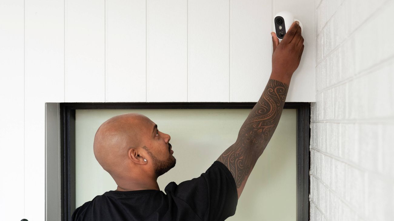 Person installing a wireless security camera above a front door.