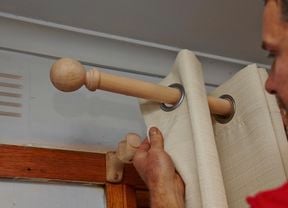 A person hanging pale coloured curtains on a curtain rod