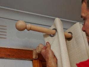 A person hanging pale coloured curtains on a curtain rod