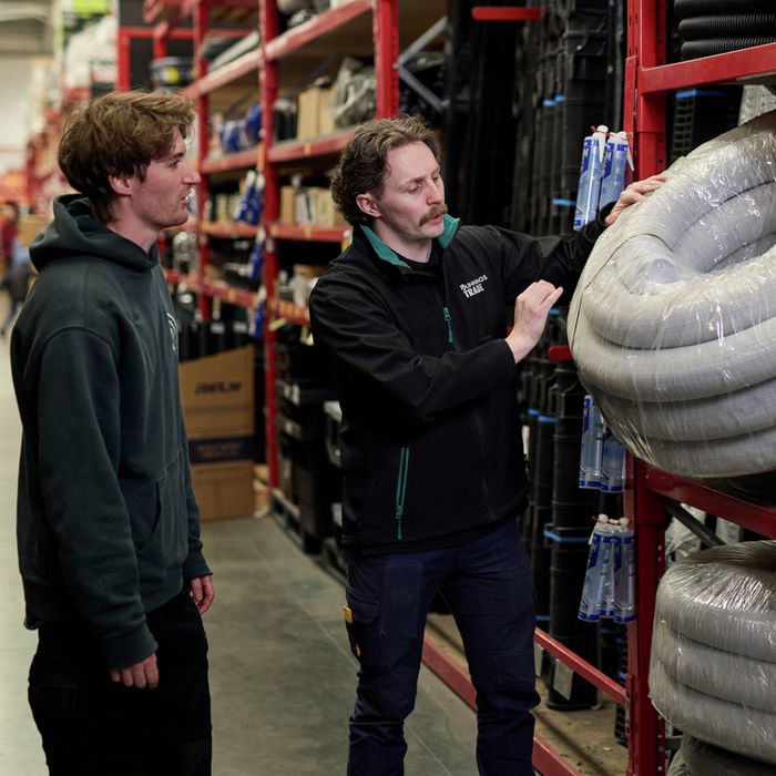 Bunnings Trade team member showing a customer a roll of flexible ducting in a store aisle.