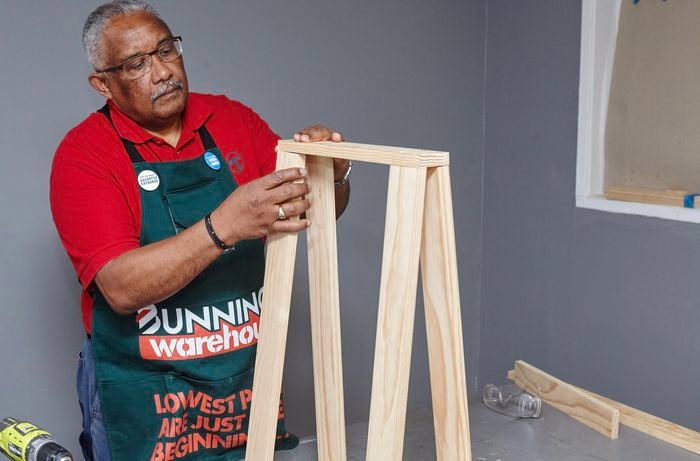 A person fitting a top piece of timber to A-frame legs