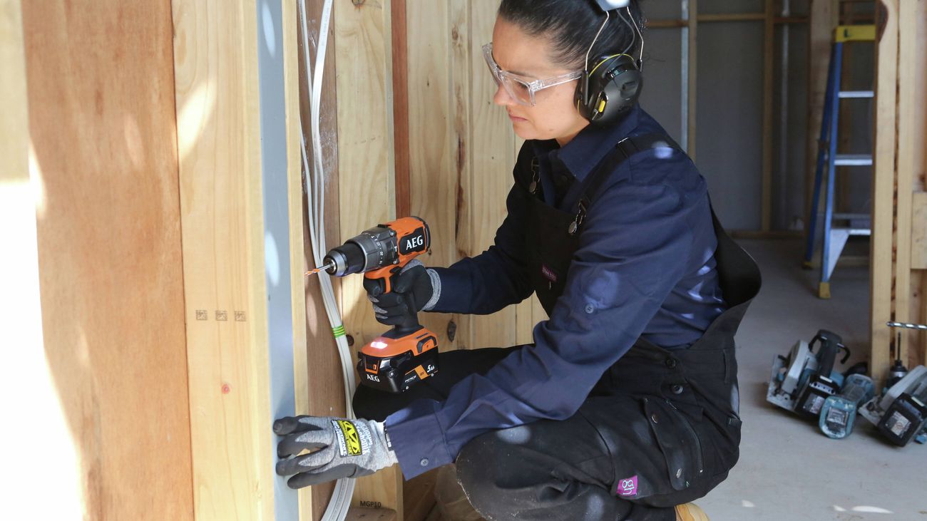 A close up of a female tradesperson wearing a Green Hip black overalls and navy blue work shirt.