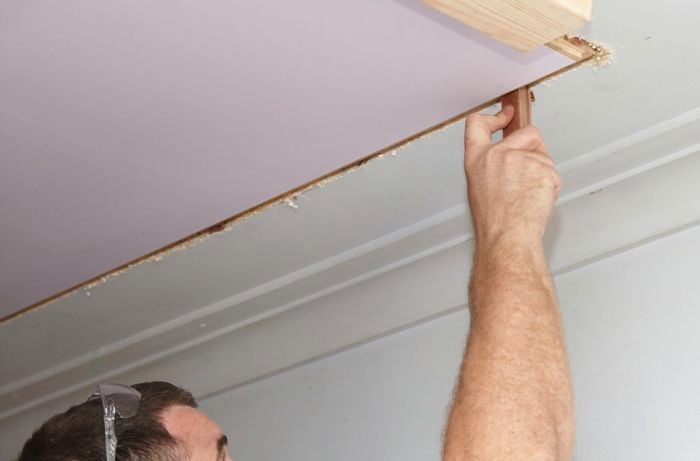 A person inserting packers into a gap between an attic ladder and a ceiling