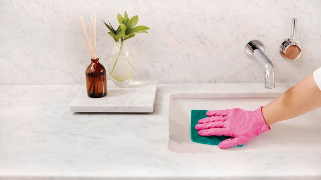 Hand in pink glove uses green cloth to wipe basin.