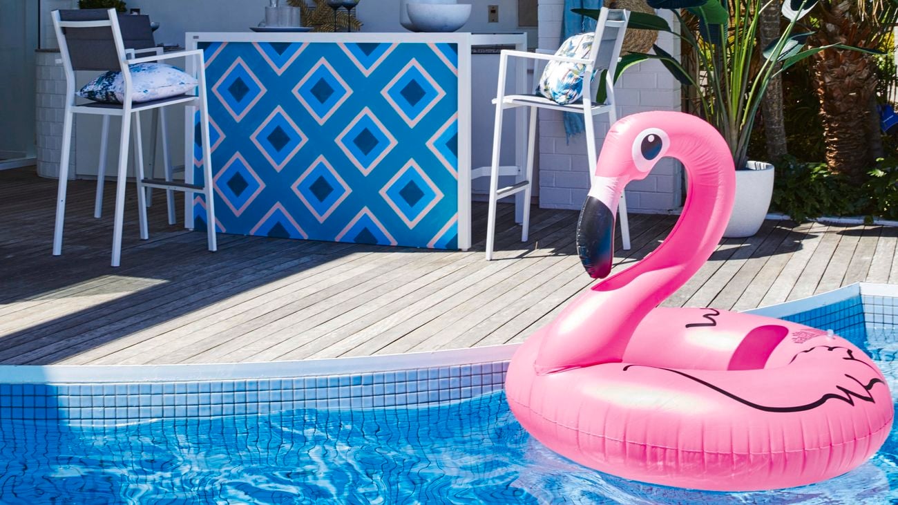 Alfresco living space including an outdoor kitchen and tiled in-ground pool. A flamingo inflatable pool toy sits in the pool