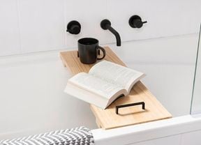 A timber shelf across a bath with a coffee cup and an open book
