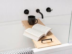 A timber shelf across a bath with a coffee cup and an open book