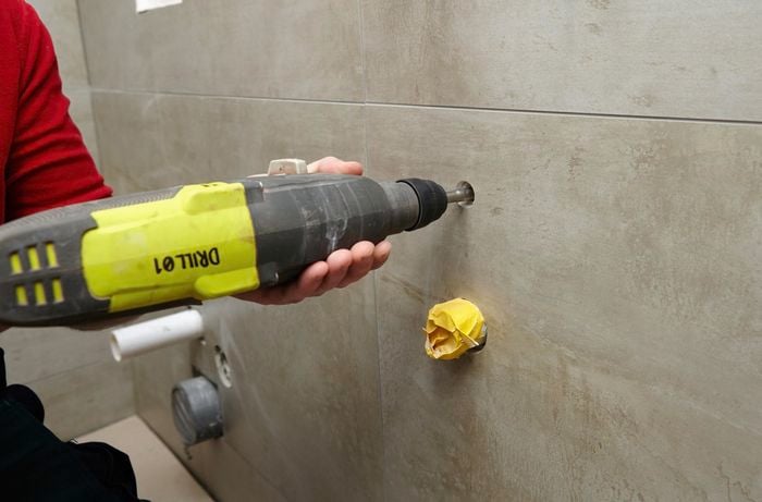 A person drilling a hole in a tiled bathroom wall
