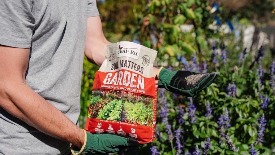 Person spreading soil matters on a garden bed.