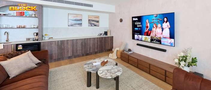 Contemporary living room featuring brown sofas, marble coffee tables, a wall-mounted TV and adjoining bar area with timber cabinetry.