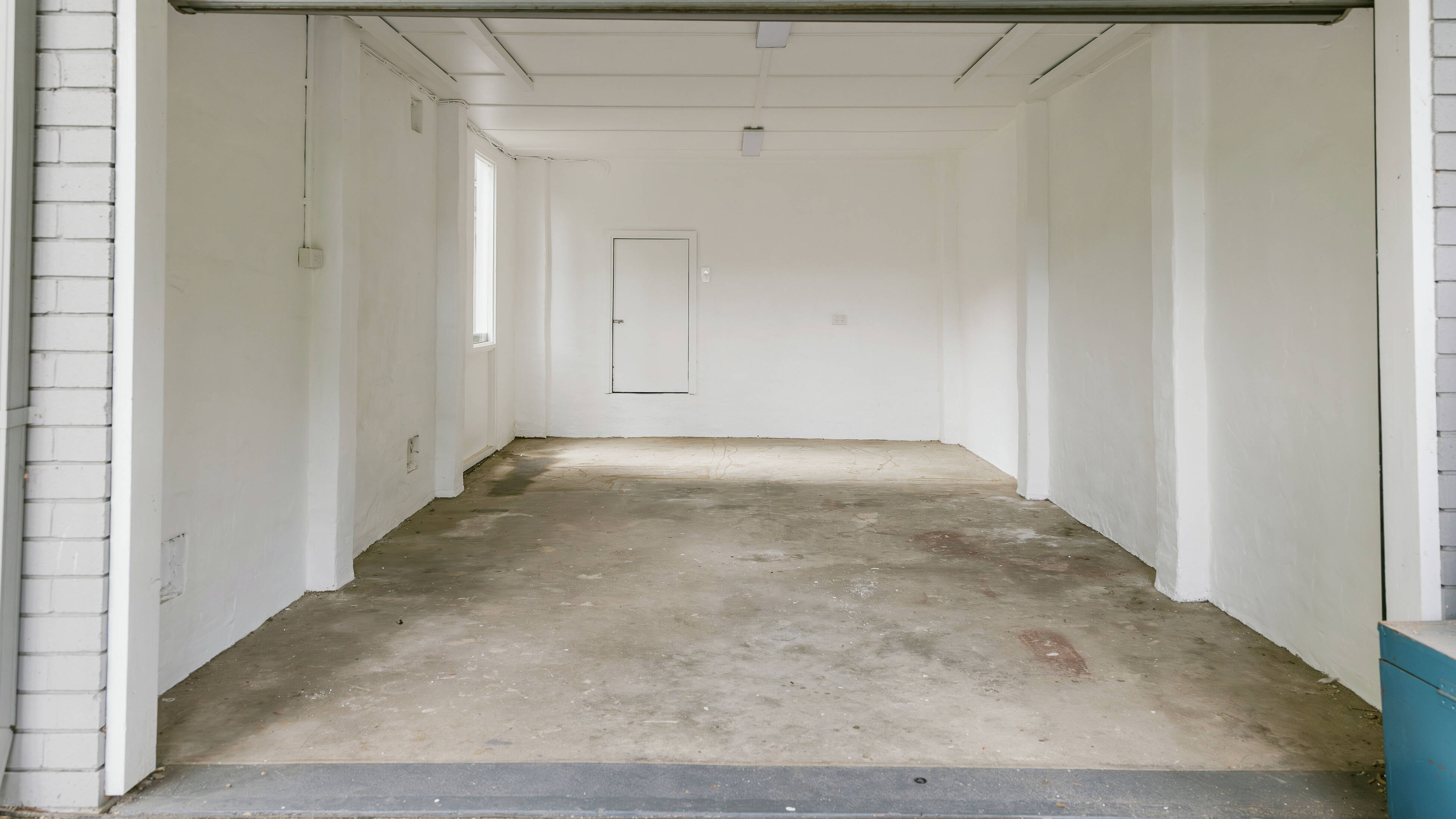 Empty freshly painted garage space with white walls and open roller door.