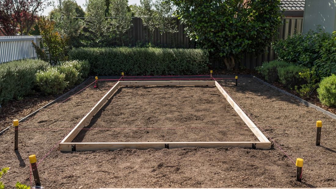 An image of a leveled rectangular area with wooden formwork, secured by stakes and red string. 