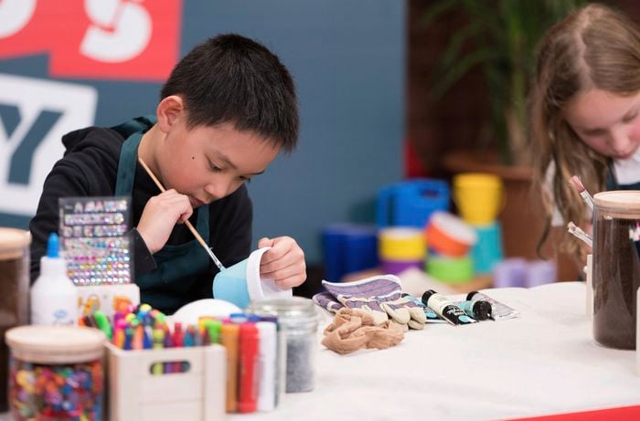 A young boy is painting a terracotta pot blue at a Bunnings DIY workshop, with craft items set aside.