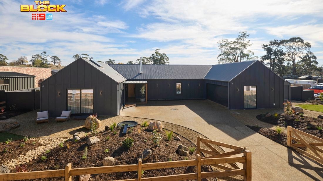 The front area of a house with rocks, shrubs, a driveway and a timber fence in it.