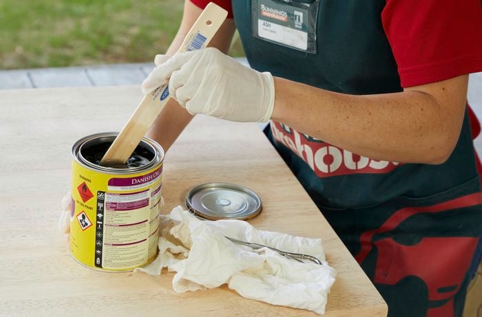 Person stirring tin of furniture oil with paint stirrer.
