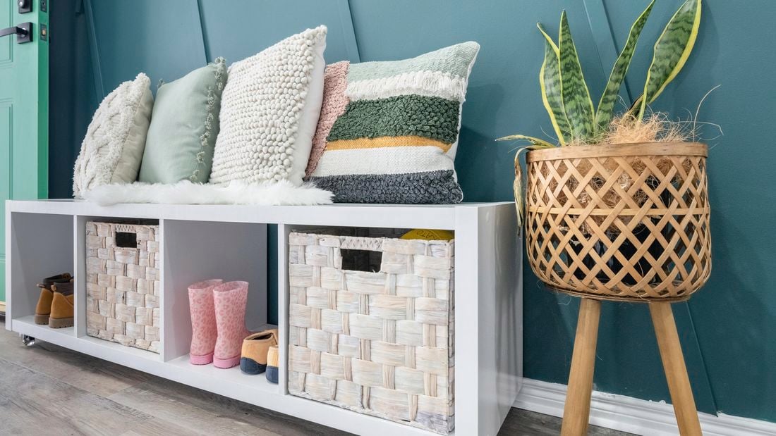 A white shelf unit with two storage cubes and shoes inside and cushions on the top