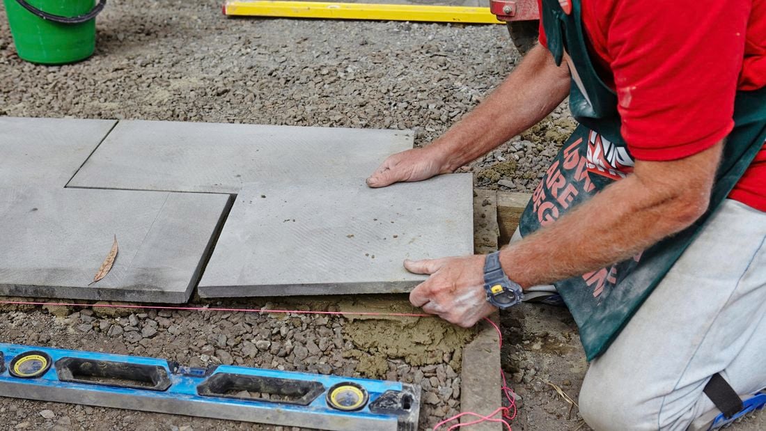 A person laying a paver on the ground alongside other pavers.
