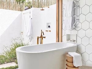 A bathroom with a white freestanding bath, tiled walls, and an outdoor shower outside the window.