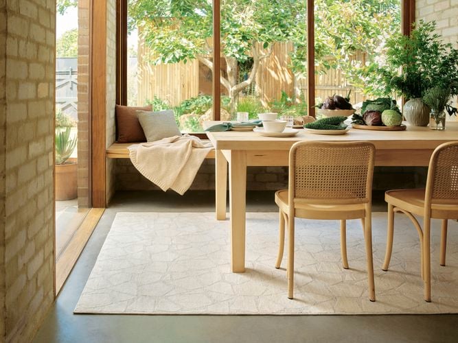 Sunlit dining area with timber table, woven chairs, and garden view