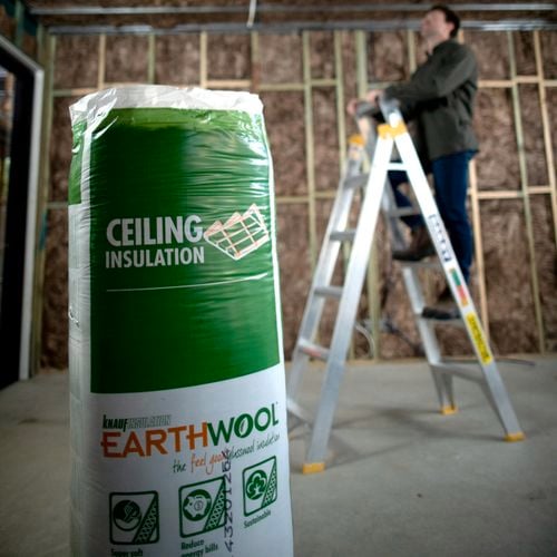 Ceiling insulation close up in package and man up on ladder in the background.