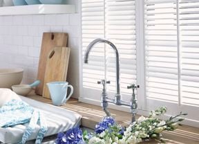 Close up of a kitchen sink and white shelves filled with blue and white dinnerware.