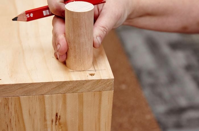 Wooden dowel legs being positioned on the underside of a kids wooden storage bench