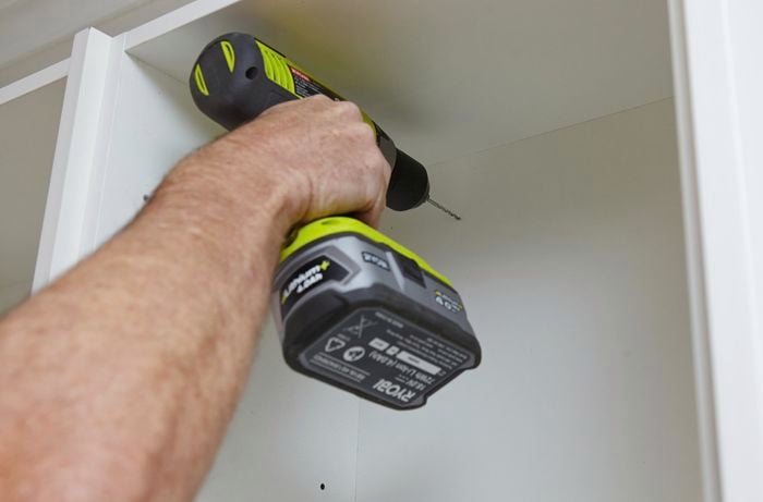 A screw being drilled into the back of a kitchen wall cabinet