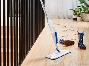 Oates Spray Mop leaning against stairwell railing, next to muddy gumboots on a timber floor.